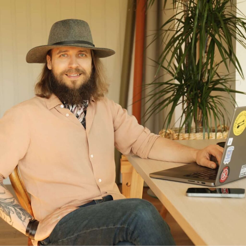 Portrait of Tanel Teemusk, AI consultant and iOS developer, in a felt hat seated at a desk with a laptop